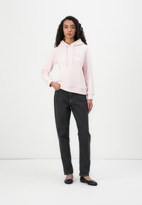 Sudadera rosa con capucha ajustable y bordado en la parte frontal, combinada con jeans gris oscuro y bailarinas negras. Tela suave y corte relajado.