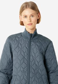 Chaqueta acolchada en azul pizarra con un alto cuello, cierre frontal y bolsillos laterales. Presenta un patrón de diamante y un diseño ligero.