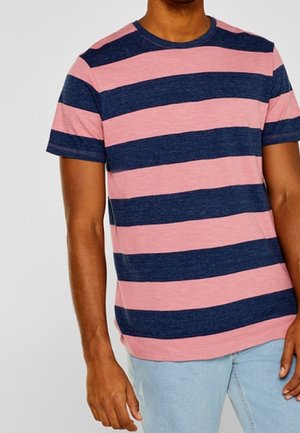Homme portant un T-shirt à manches courtes à col rond avec de larges rayures horizontales bleu marine et rose, associé à un jean bleu clair.