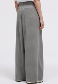 Gray pinstriped wide-leg trousers with a high waist, featuring two back pockets and a textured fabric, worn with white sneakers.
