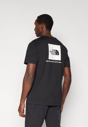 Camiseta negra de manga corta con un gran cuadrado blanco que lleva el logotipo de "THE NORTH FACE" y el texto "NEVER STOP EXPLORING" en la parte trasera.