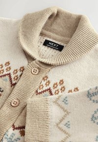 Cardigan beige avec un col châle côtelé et une fermeture à boutons. Présente des motifs de tricot texturés en marron et bleu sur le devant.