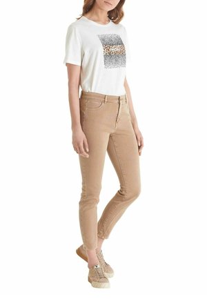 Camiseta blanca con un gráfico de estampado de leopardo, combinada con jeans ajustados beige y zapatillas de deporte marrón claro. Diseño simple con mangas cortas.