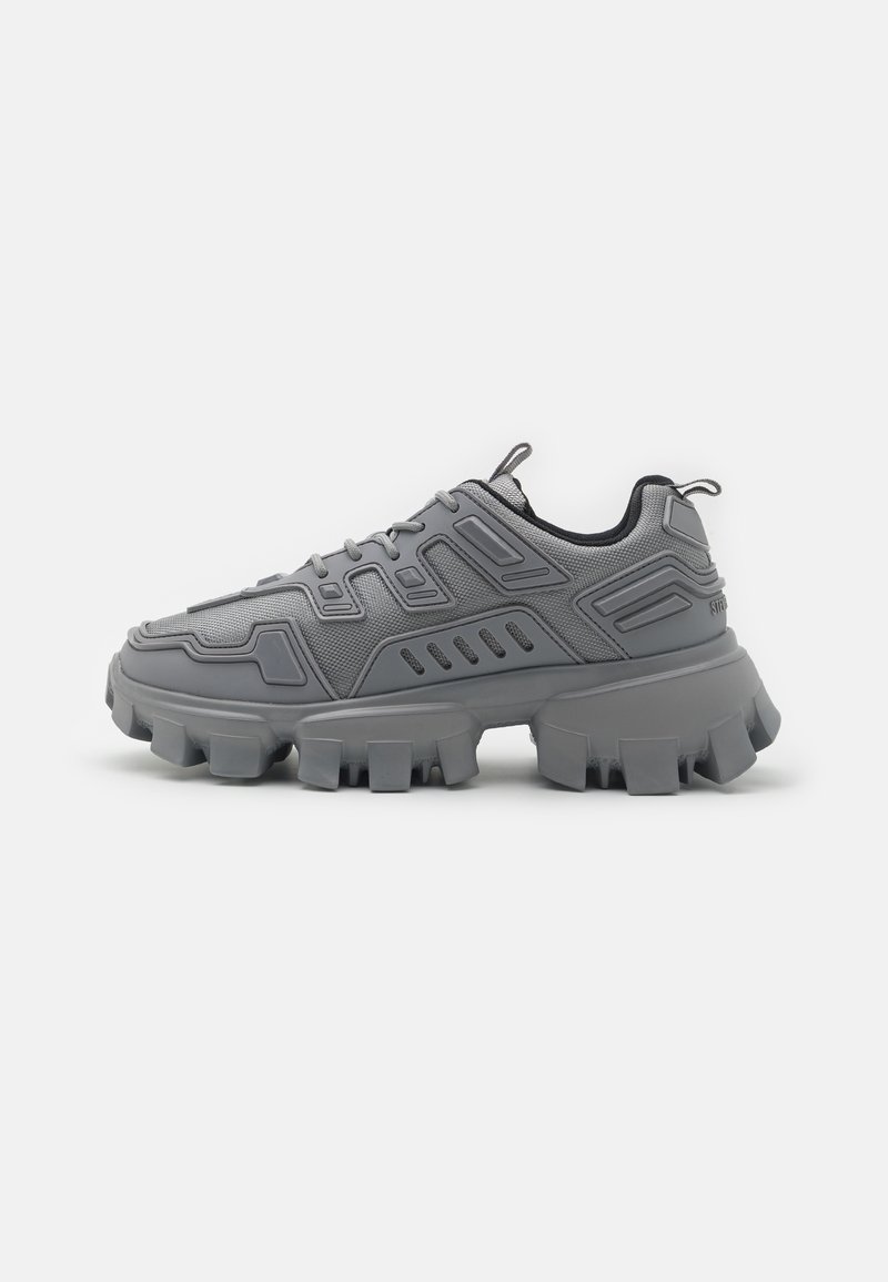 Gray sneakers with a textured mesh upper, distinct molded design elements, and a thick, chunky outsole with a lug pattern.