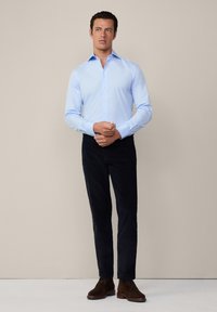 Camisa abotonada de color azul claro con mangas largas, combinada con pantalones oscuros y botas de ante marrones. Diseño simple, sin patrones visibles.