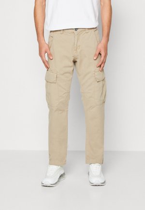 Pantaloni cargo bej cu buzunare laterale, croială dreaptă și tivuri răsucite, din material de bumbac. Purtați cu adidași albi.