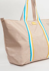 Grande borsa tote beige realizzata in materiale lucido, con strisce verticali blu, gialle e bianche, dotata di manici resistenti e una patch con logo.