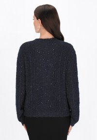 Navy blue neulepusero, jossa on teksturoitu muotoilu, löysä istuvuus, pyöreä pääntie ja hajallaan olevat vaaleat yksityiskohdat, esittelee kotoisan, kerroksittaisen ilmeen.