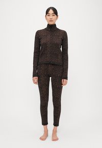 Čierny a hnedý leopardí vzor športového oblečenia, ktorý zahŕňa dlhý top na zips s dlhým rukávom a priliehavé legíny s logovanými detailmi na lemoch.