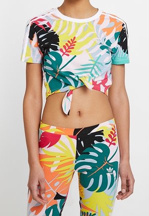 Kolorowy krótki T-shirt z tropikalnymi wzorami liści w zielonym, różowym i żółtym kolorze; zawiązany z przodu. Dopasowane legginsy o podobnym wzorze.