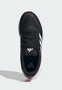 Basket noir de sport avec tige en mesh, logo trois rayures blanches et accents rouges. Dispose d'un laçage traditionnel et d'une semelle blanche rembourrée.