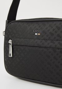 Borsa a spalla nera con texture e motivo geometrico, hardware in argento, logo "BOSS" in evidenza e tasca anteriore con zip.