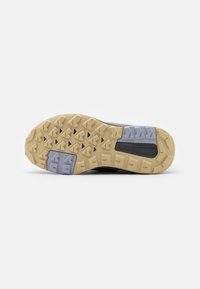 Semelle extérieure d'une chaussure de randonnée avec des crampons en caoutchouc beige et gris, des rainures profondes pour l'adhérence, et le texte "TRAXION" près du talon.