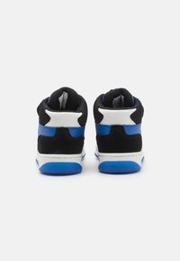 Zapatillas altas que presentan malla negra y detalles de gamuza azul, con un acabado blanco y suela de goma azul. La vista trasera muestra un cuello acolchado.