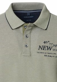 Zielona koszulka polo z teksturowanej tkaniny, z kontrastowym kołnierzykiem, trzema guzikami oraz haftowanym tekstem z detalami współrzędnych Nowego Jorku i lokalizacji.