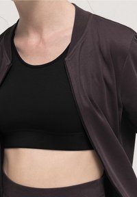 Mörklila, lätt bomberjacka med en slät textur. Bärs över en svart linne, vilket visar en kortad design och minimala detaljer.