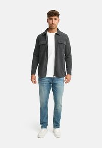 Grå button-up skjorte med to brystlommer, parret med en hvid t-shirt og lyseblå jeans, yderligere suppleret med hvide sneakers.