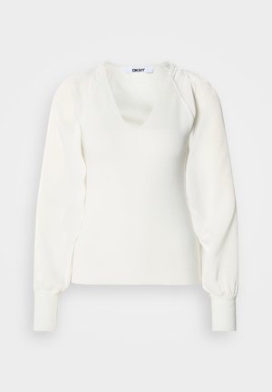 Witte, lange mouw, gebreide top met een geribbelde stof, geplooide mouwen die bij de manchetten zijn samengebonden, en een V-hals met een DKNY-label aan de kraag.