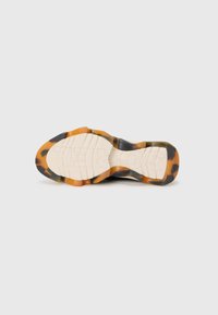 Sålen på en sneaker med et sort og orange skildpadde-mønster, med teksturerede riller og ordet "SOLE" synligt.