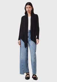 Black knit cardigan with an open front and ribbed texture, paired with light blue wide-leg jeans and black flat shoes.