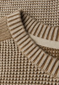 Beige gebreide trui met een gestructureerd wafelpatroon en ribgebreide manchetten in een lichtere tint, met een gelaagd ontwerp.