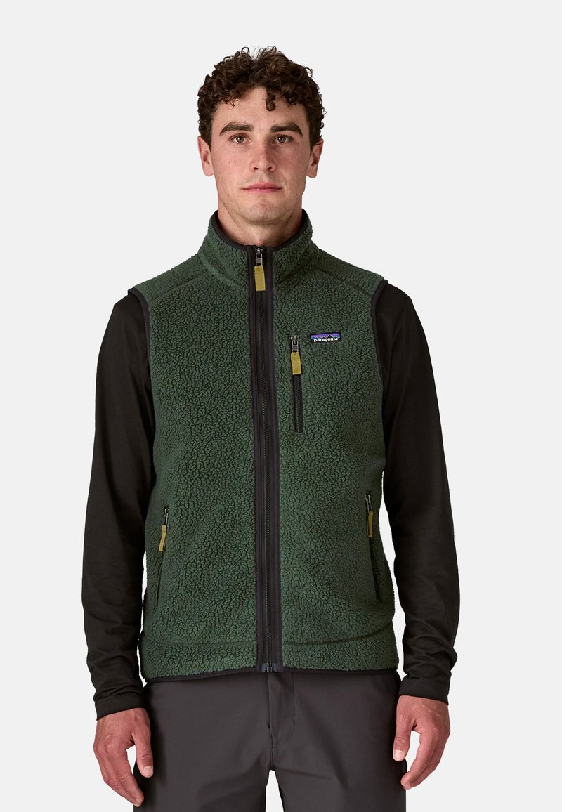 Gilet in pile verde con colletto alto, zip frontale e maniche lunghe nere. Presenta tasche con zip e tiranti gialli. Materiale texturizzato.
