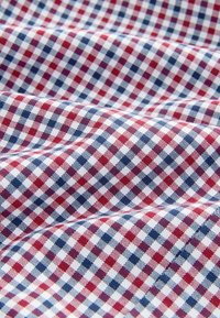 Baumwollstoff mit einem rot-weiß-blauen karierten Muster. Präsentiert kleine, regelmäßig angeordnete Quadrate. Weiche Textur mit einem leichten Glanz.