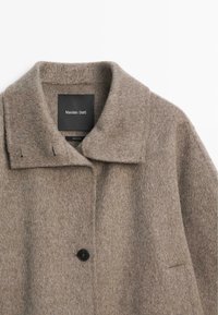 Wełniany płaszcz w jasnobrązowym kolorze z klapowym kołnierzem, czarnym zapięciem na guziki i dwoma przednimi kieszeniami. Metka z napisem „Massimo Dutti”. Miękka tekstura.