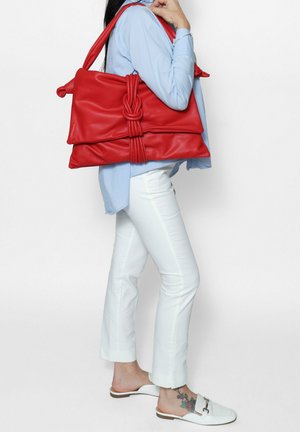 Borsa a tracolla in pelle rossa con un design a nodo, dotata di due ampi scomparti e una texture liscia e morbida. Stilizzata con una tracolla.
