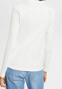 Vit ribbad långärmad topp med en figurnära design och krage, tillsammans med ljusblå denimjeans med bakfickor och avkopplad passform.