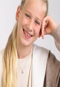 Silberne herzförmige Ohrringe, eine zarte Halskette mit einem Doppelherz-Anhänger, ein hellbrauner Cardigan und ein beiges Oberteil. Helle Haut und lange blonde Haare.
