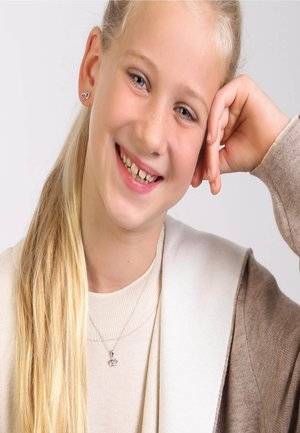 Silberne herzförmige Ohrringe, eine zarte Halskette mit einem Doppelherz-Anhänger, ein hellbrauner Cardigan und ein beiges Oberteil. Helle Haut und lange blonde Haare.