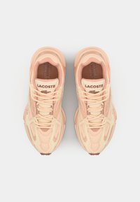 Tenisky Lacoste v broskvové a krémové barvě s panelováním z pleteniny a semiše, s kulatou špičkou, šněrovacím designem a značenými detaily na jazyku.