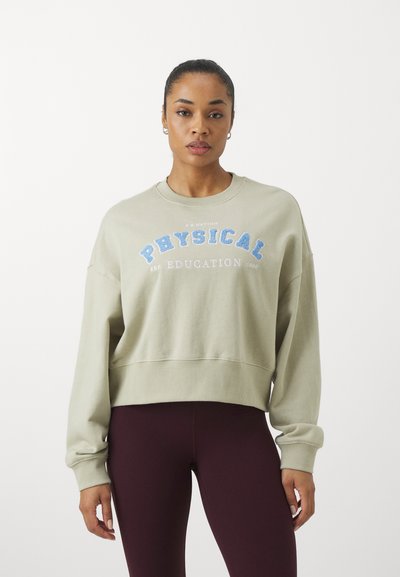 Light green cropped sweatshirt with “PHYSICAL EDUCATION 1990” text in blue, round neckline, and long sleeves. Soft material and relaxed fit.