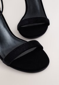 Crne sandale s potpeticom od glatke kože s mekanim velur remenčićem. Dizajn s otvorenim vrhom, elegantnog silueta i minimalističkih detalja.