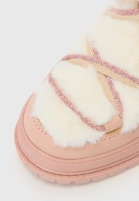 Rosa lädersko med fuskpäls ovanför och flätade rosa snören. Har en rund tå och en texturerad sula för bra grepp.