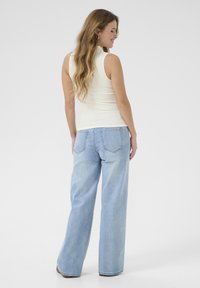Top senza maniche avorio abbinato a jeans a gamba larga di colore blu chiaro. I jeans presentano tasche posteriori e una vita regolare.