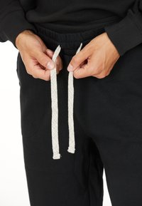 Händer som justerar vita dragskor på svarta sweatpants med elastisk midja, tillsammans med en svart långärmad tröja.