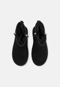 Sorte ankelstøvler i nubuck med myk pelsinnside, doble sideglidelåser og teksturerte såler for bedre grep.