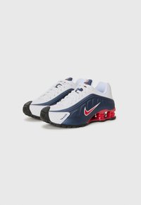 Nike-sneakers med en hvit mesh-overdel med marineblå og røde detaljer, teksturerte overlegg og en svart gummisåle med fjæraktig rød demping.