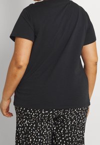 Camiseta de algodón de manga corta negra. Presenta un cuello redondo y un corte relajado. Se combina con pantalones de patrones de puntos en blanco y negro.