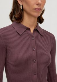 Gebreide, ribbelige top in gematigd paars met een kraaghalslijn en knoopsluiting. Beschikt over lange mouwen en een gestructureerde stof voor extra detail.