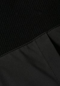 Tessuto a maglia nero nella parte superiore con una texture a costine, che si trasforma in un tessuto nero opaco e liscio nella parte inferiore, caratterizzato da cuciture ordinate lungo la cucitura.