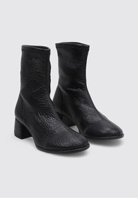 Botas de tobillo de cuero negro con superficie texturizada, tacón bloque, punta afilada y sin características visibles de cierre o adornos.
