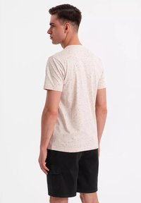 Lichtbeige t-shirt met verspreide zwarte spikkels, korte mouwen en een ronde hals, gecombineerd met zwarte shorts met zijzakken.