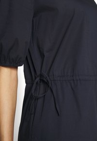 Mörkblå klänning med elastiska puffärmar, en dragsko i midjan för justering, samt ett mjukt, lätt tyg med en subtil lyster.