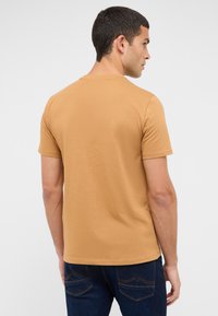 Short-sleeve t-shirt in a warm, tan color. Smooth cotton fabric, classic fit with a crew neck and plain back design. Paired with dark jeans.