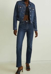 Dark denim jacket with silver buttons, two chest pockets, and matching fitted jeans. Model wearing black crop top and heeled sandals.