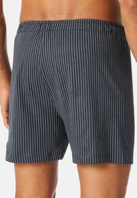 Boxers bleu marine avec des rayures verticales blanches, ceinture élastique et texture de tissu douce. Design simpliste sans matériel ou accents visibles.
