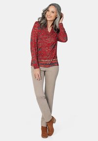 Rotes Langarmhemd mit floralem Muster, kombiniert mit hellbeigen Hosen und braunen Stiefeletten. Entspannte Passform und subtil strukturierter Stoff.
